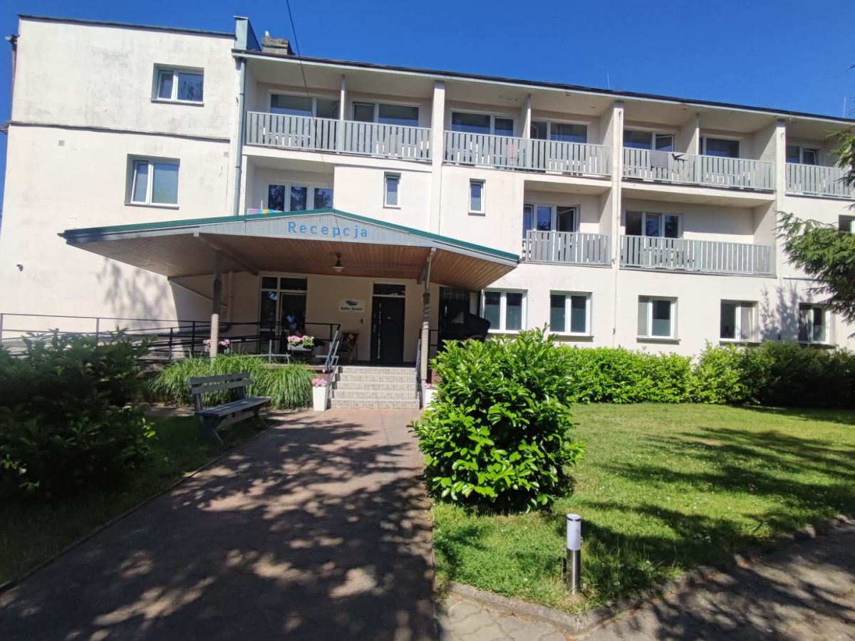 Budynek ośrodka Baltic Resort w Darłówku z zadaszonym wejściem do recepcji, balkonami i zielonym ogrodem