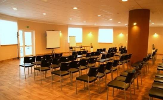 Sala wielofunkcyjna Baltic Resort ustawiona pod szkolenie: rzędy krzeseł, ekran projekcyjny i flipchart, drewniana podłoga i duże okna
